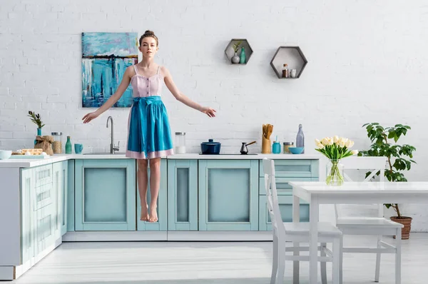 Belle fille pieds nus dans tablier lévitant dans l'air dans la cuisine — Photo de stock