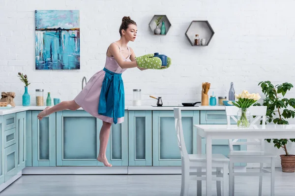 Bella ragazza scalza in presine levitante in aria con pentola in cucina — Foto stock