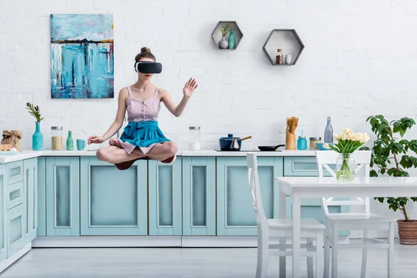 Молода жінка вирівнюється в повітрі в гарнітурі віртуальної реальності і жестикулює на кухні — стокове фото