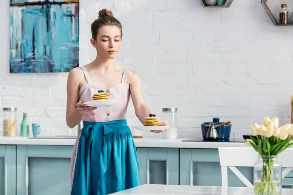 Selective focus of focused elegant girl in apron serving tasty pancakes in kitchen — Stock Photo