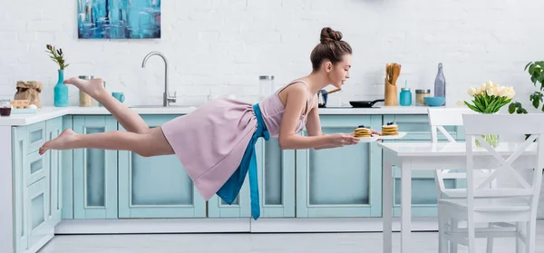 Junge glückliche barfüßige Frau fliegt in der Luft, während sie leckere Pfannkuchen serviert — Stockfoto
