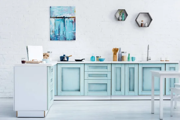 Interior de la moderna cocina de color turquesa brillante con pintura en la pared de ladrillo blanco - foto de stock