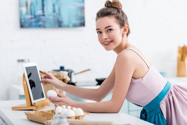 Mujer feliz joven usando tableta digital con pantalla en blanco mientras sostiene el huevo - foto de stock