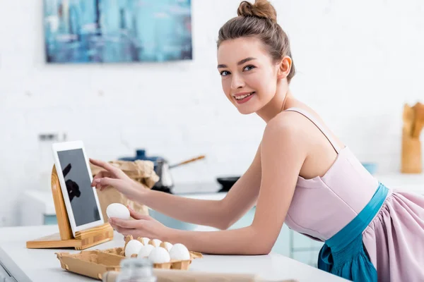 Jovem mulher feliz usando tablet digital com tela em branco enquanto segurando ovo — Fotografia de Stock
