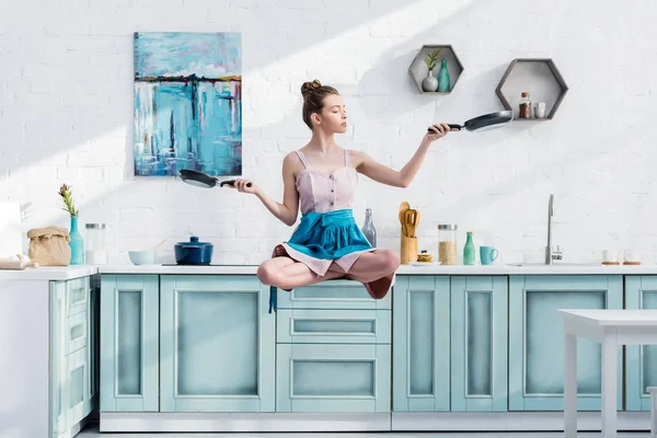 Young woman levitating in air in lotus pose with pans in hands — Stock Photo