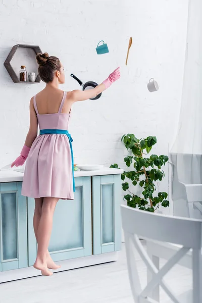 Молода елегантна жінка в гумових рукавичках вирівнюється в повітрі з посудом для приготування їжі на кухні — стокове фото