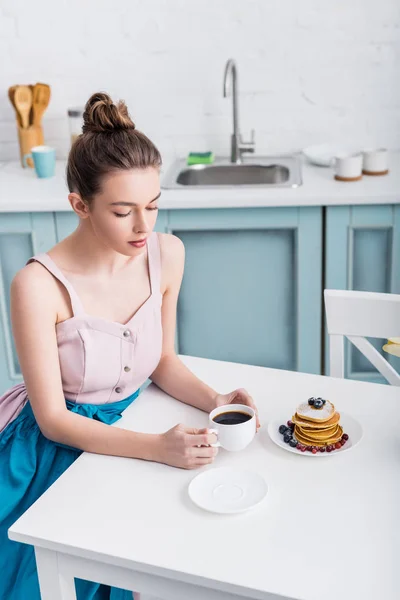 Attractive elegant young woman sitting at table and drinking coffee — Stock Photo