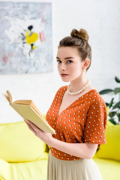 Attraktive elegante junge Frau hält Buch in der Hand und blickt in die Kamera — Stockfoto