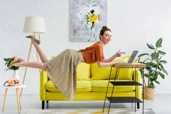 Elegante junge Frau schwebt in der Luft und zeigt mit dem Finger auf Laptop — Stockfoto