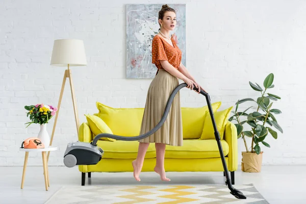 Elegant barefoot young woman levitating in air while vacuuming carpet — Stock Photo