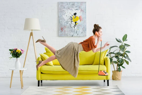 Vista laterale di elegante giovane donna levitante in aria e parlando al telefono vintage in soggiorno — Foto stock