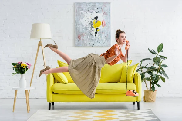 Вид сбоку счастливой элегантной молодой женщины, левитающей в воздухе и разговаривающей по винтажному телефону в гостиной — стоковое фото