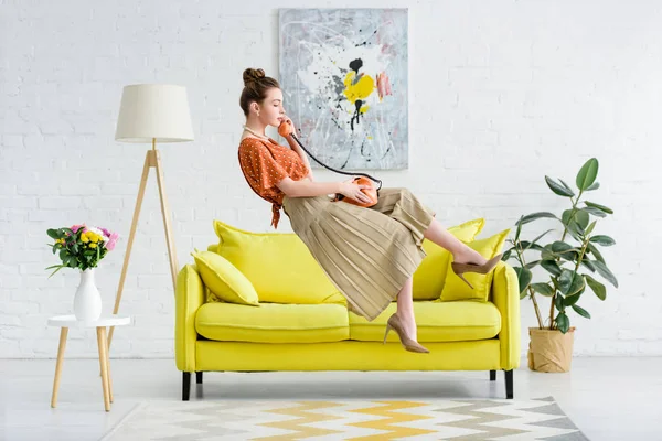 Seitenansicht einer eleganten jungen Frau, die in der Luft schwebt und im Wohnzimmer auf einem Vintage-Telefon spricht — Stockfoto