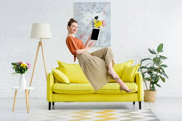 Elegante, glückliche junge Frau schwebt in der Luft und zeigt ein digitales Tablet mit leerem Bildschirm im Wohnzimmer — Stockfoto