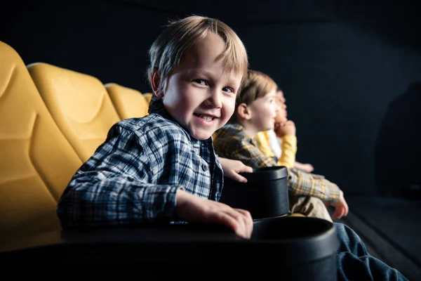 Mignon garçon regardant caméra tout en étant assis avec des amis au cinéma — Photo de stock