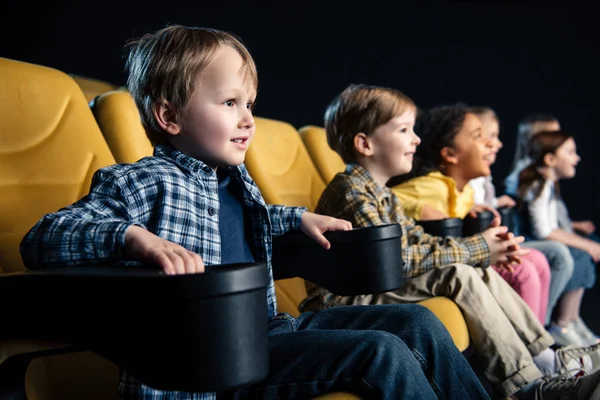 Foco seletivo de amigos multiculturais sorridentes sentados no cinema e assistindo filme — Fotografia de Stock