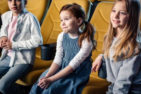 Tres lindos niños sentados en el cine y viendo películas - foto de stock