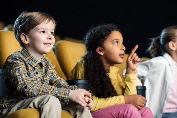 Lindo africano americano niño apuntando con el dedo mientras viendo la película con amigos en el cine - foto de stock