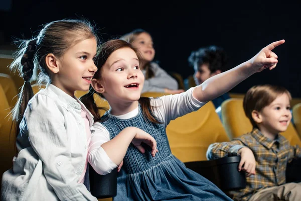 Niño emocionado señalando con el dedo mientras ve la película en el cine junto con amigos multiculturales - foto de stock