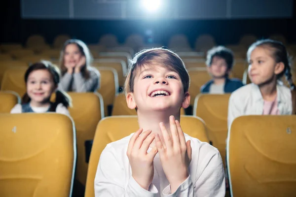 Sonriente chico emocional viendo película en el cine junto con amigos multiculturales - foto de stock
