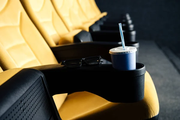 Selective focus of orange cinema seats with disposable cup in cup holder — Stock Photo