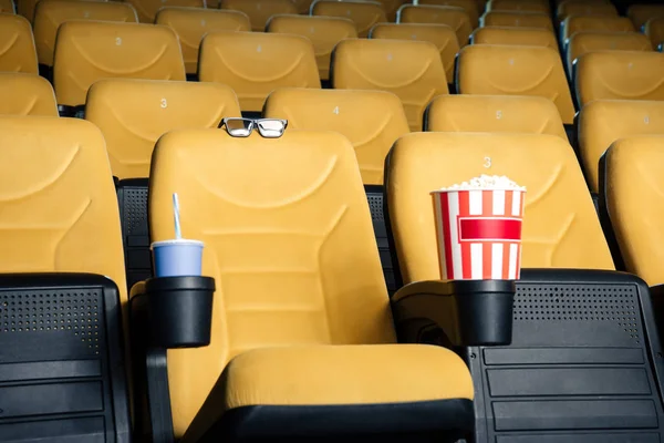 Assentos de cinema laranja com copos de papel de refrigerante e pipoca em suportes de xícara, e óculos 3d — Fotografia de Stock