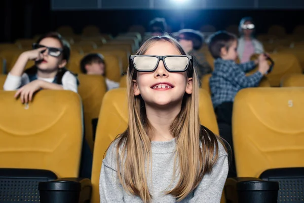 Messa a fuoco selettiva di carino bambino sorridente in occhiali 3d seduto con gli amici nel cinema — Foto stock