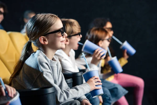 Foco seletivo de amigo multicultural sentado no cinema com copos de papel e assistindo filme — Fotografia de Stock