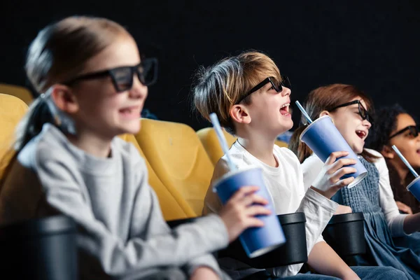 Selektiver Fokus fröhlicher multikultureller Freunde in 3D-Brillen, die sich Filme ansehen und Pappbecher in der Hand halten — Stockfoto