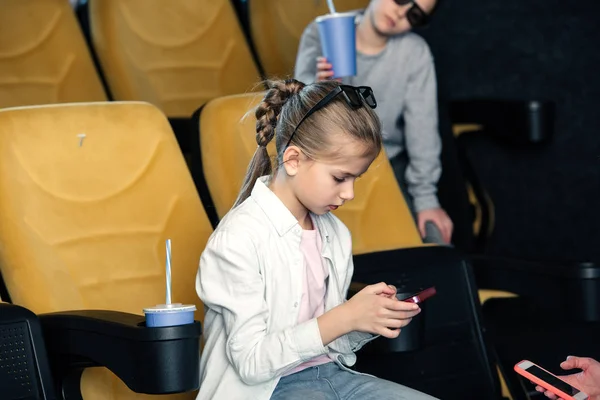 Selective focus of cute child using smartphone while spending time in cinema together with friends — Stock Photo