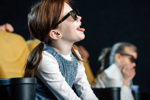 Foyer sélectif de mignon enfant montrant la langue tout en étant assis au cinéma — Photo de stock