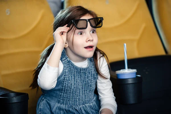 Lindo niño sorprendido viendo película en el cine mientras está sentado cerca de la taza de papel - foto de stock