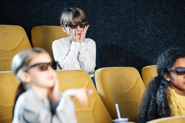 Foco seletivo de menino preocupado de mãos dadas no rosto enquanto assiste filme junto com amigos multiculturais — Fotografia de Stock