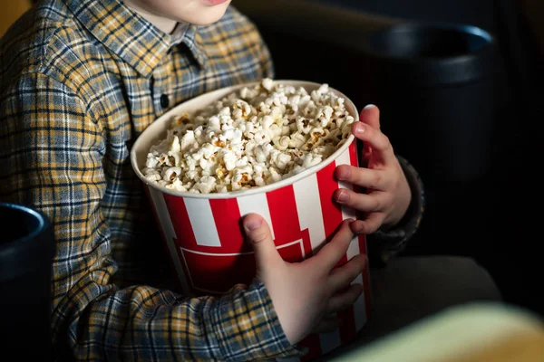 Vista parziale del ragazzo che tiene in mano la tazza di carta con popcorn mentre è seduto al cinema — Foto stock