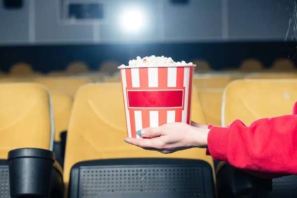 Partial view of child holding stripped paper cup with popcorn in cinema — Stock Photo