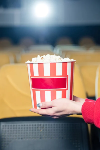 Partial view of child holding stripped paper cup with popcorn in cinema — Stock Photo