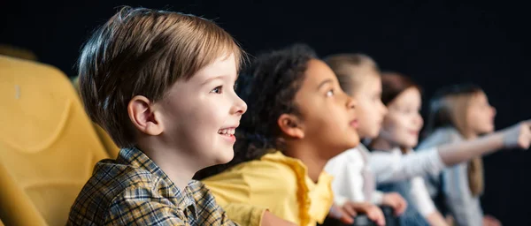 Panoramic shot of multicultural friends watching movie in cinema together — Stock Photo