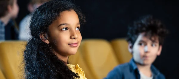 Панорамный снимок африканского американского ребенка, смотрящего фильм вместе с другом смешанной расы — стоковое фото
