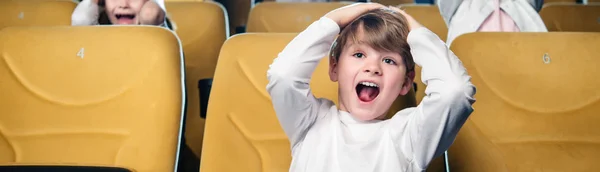 Plan panoramique de garçon excité criant tout en regardant un film au cinéma — Photo de stock