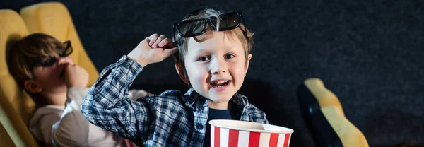 Tiro panorâmico de menino bonito olhando para a câmera e segurando copo de papel despojado com milho pop — Fotografia de Stock