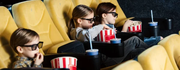 Panoramica di bambini che guardano film in bicchieri 3d e mangiano popcorn al cinema — Foto stock