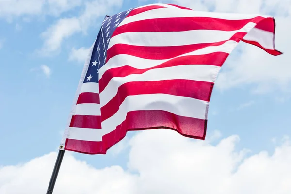 Vista en ángulo bajo de la bandera de EE.UU. con estrellas y rayas contra el cielo azul con nubes - foto de stock