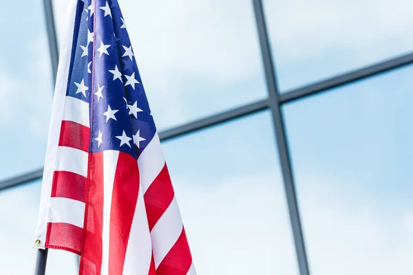 Sterne und Streifen auf amerikanischer Flagge in der Nähe von Gebäuden mit Himmelsspiegelung an Fenstern — Stockfoto