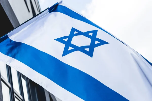 Низкоугольный вид национального флага Израиля со звездой Дэвида рядом со зданием против неба — стоковое фото