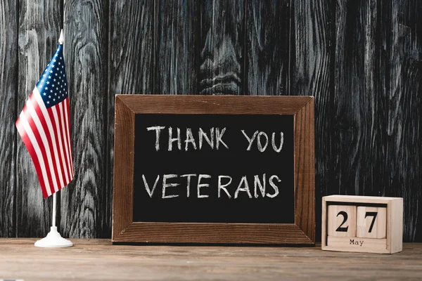 Чорна дошка з подякою вам ветерани, що пропускають біля американського прапора і кубиків з датою — стокове фото