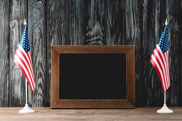 Empty black board near american flags with stars and stripes — Stock Photo