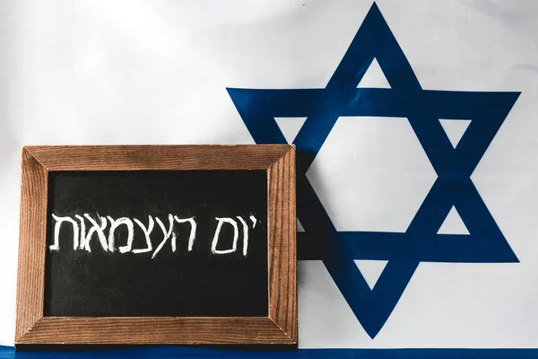 Chalkboard with hebrew lettering near blue star of david on national flag of israel — Stock Photo