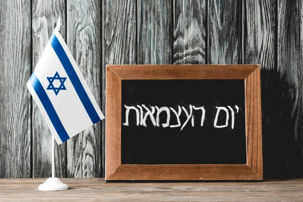 Pizarra con letras hebreas cerca de la bandera nacional de Israel con estrella azul de David - foto de stock