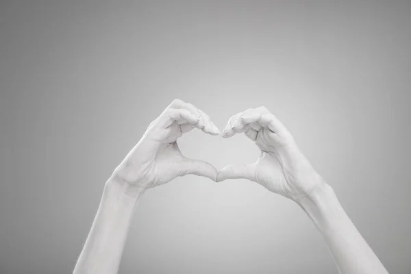 Vista recortada de las manos femeninas pintadas de blanco mostrando el signo en forma de corazón en gris - foto de stock