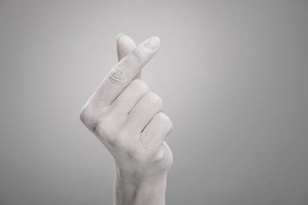 Cropped view of female hand painted in white showing heart-shaped sign on grey — Stock Photo